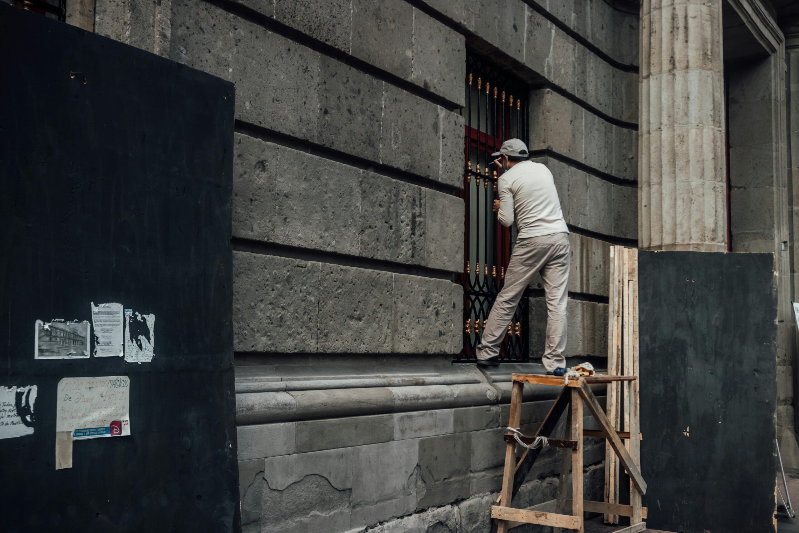 A man painting the exterior of a historic building in Mexico City, standing on a wooden ladder.